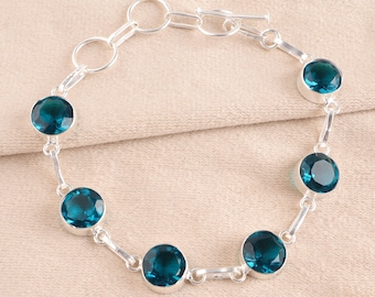 May include: A silver chain bracelet featuring five round, faceted dark blue stones set in polished silver bezels. The bracelet includes a toggle clasp mechanism with a circular ring and a T-bar connector, creating a continuous link design.