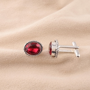 May include: A pair of silver cufflinks with red gemstone accents. The cufflinks have a rope-like design around the edges.