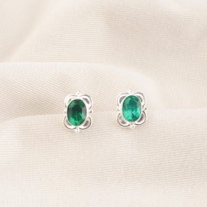 Puede incluir: Un par de pendientes de plata con piedras preciosas ovaladas verdes engastadas en un diseño floral decorativo.