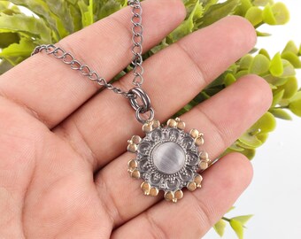 May include: A silver-tone necklace with a circular pendant. The pendant features a central, light-colored stone surrounded by a detailed, floral-like design with gold-colored accents. The chain is a dark silver color.