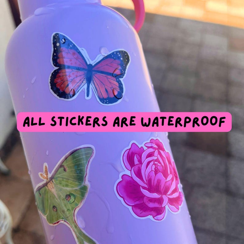 May include: A light purple water bottle decorated with three stickers: a pink and black butterfly, a green moth, and a bright pink flower. A pink horizontal banner across the center displays the black text: ALL STICKERS ARE WATERPROOF.
