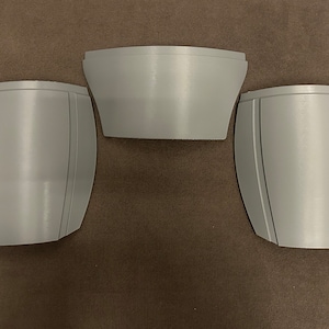 May include: Three gray plastic pieces for a costume or cosplay. The pieces are shaped like a chest piece and two arm pieces.