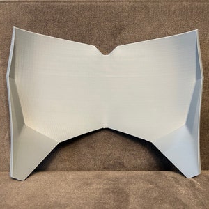 Pu&ograve; includere: Un oggetto grigio, di forma geometrica, stampato in 3D con una superficie piatta e un bordo appuntito. L'oggetto &egrave; in plastica e ha una finitura liscia.
