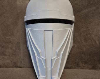 May include: A light gray, 3D-printed helmet with a rounded top and angular face design. The helmet features a black visor and detailed geometric patterns. The overall design suggests a futuristic or sci-fi theme.