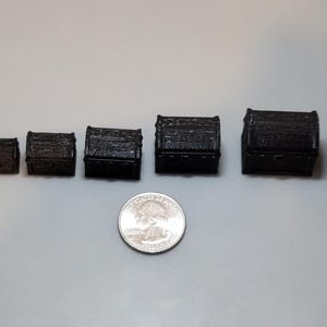 May include: A set of ten black wooden treasure chests of varying sizes, ranging from small to large. The chests are arranged in a row from smallest to largest. A silver US quarter is included for scale.