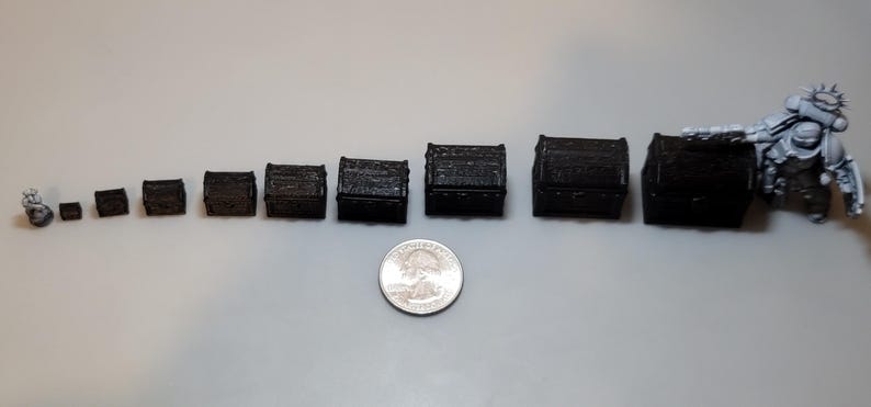 Puede incluir: Un conjunto de diez cofres del tesoro de madera negra de diferentes tama&ntilde;os, que van desde peque&ntilde;os hasta grandes. Los cofres est&aacute;n dispuestos en una fila desde el m&aacute;s peque&ntilde;o hasta el m&aacute;s grande. Una moneda de 25 c&eacute;ntimos de euro plateada se incluye para la escala.