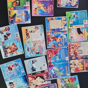 May include: A collection of vintage VHS tapes featuring animated Disney movies. Titles include "The Lion King," "Cinderella," "Mulan," "Frozen," and "Hercules." The tapes are arranged on a dark surface, showcasing their colorful cover art.