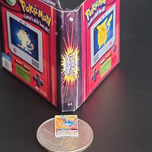 May include: A miniature Pok&eacute;mon-themed binder featuring red and black graphics with images of Meowth and Pikachu on the front panels. A tiny, rectangular Pok&eacute;mon trading card rests on top of a United States quarter coin for scale comparison.
