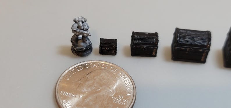 Puede incluir: Una figurita miniatura pintada de gris de un marine espacial sosteniendo un arma, junto a cuatro cofres de madera negra en miniatura de diferentes tama&ntilde;os. Se incluye una moneda de 25 centavos de d&oacute;lar estadounidense para la escala.
