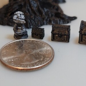 Puede incluir: Una colecci&oacute;n de cofres del tesoro en miniatura, algunos con detalles intrincados, y una peque&ntilde;a figura gris detallada. Los cofres son de varios tama&ntilde;os y est&aacute;n hechos de un material oscuro y texturizado. Se incluye una moneda de 25 centavos de d&oacute;lar estadounidense para la escala.