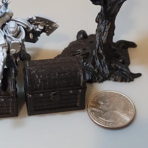 Puede incluir: Cuatro cofres del tesoro de madera en miniatura de varios tama&ntilde;os, pintados de marr&oacute;n con un aspecto desgastado. Los cofres est&aacute;n dispuestos en fila del m&aacute;s grande al m&aacute;s peque&ntilde;o. Una figura en miniatura de un marine espacial se encuentra detr&aacute;s de los cofres.