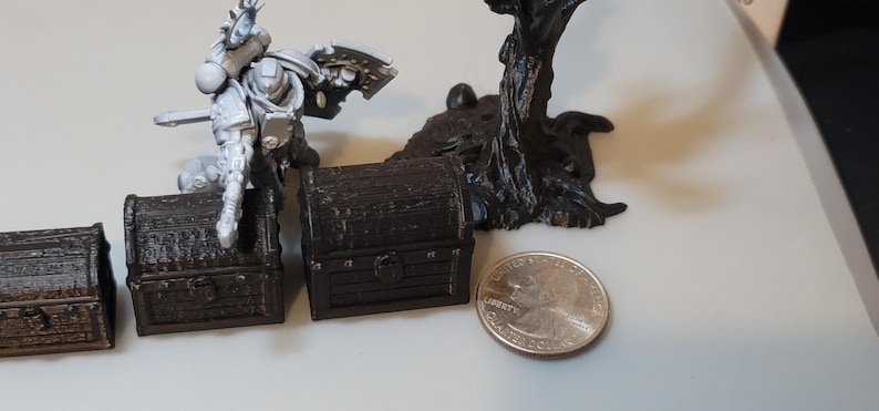 Puede incluir: Cuatro cofres del tesoro de madera en miniatura de varios tama&ntilde;os, pintados de marr&oacute;n con un aspecto desgastado. Los cofres est&aacute;n dispuestos en fila del m&aacute;s grande al m&aacute;s peque&ntilde;o. Una figura en miniatura de un marine espacial se encuentra detr&aacute;s de los cofres.