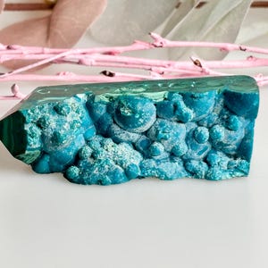 Op de afbeelding: Een tealblauw en groen malachietkristal met een unieke, bubbelige textuur. Het kristal is een natuurlijke formatie en heeft een ruw, onregelmatig oppervlak.