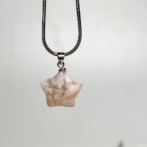 Op de afbeelding: Een zilveren ketting met een roze en witte agaat ster hanger.