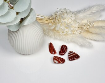 May include: Five red and white striped agate stones on a white surface. The stones are smooth and polished.