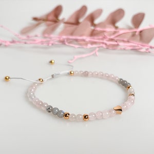 Peut inclure: Un bracelet délicat composé de perles roses et grises, rehaussé de perles dorées et d'un charm en forme de cœur doré.