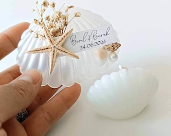 May include: White seashell with a starfish, dried flowers, and a small seashell inside. A white card with the text "Beril & Burak 24.06.2024" is attached to the seashell.