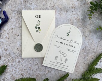May include: A white wedding invitation with a green floral design and the text "Mitlalagamage Deatlainy GAMZE & ENES" in black cursive script. The invitation includes the names of the bride and groom's families, the date of the wedding, and the location of the ceremony.