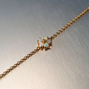 Puede incluir: Un delicado collar de oro con un colgante floral. El colgante está formado por pequeñas ópalos, cada uno mostrando un juego de colores. La cadena es fina y el diseño es minimalista. Los ópalos están engastados en un engaste de oro.