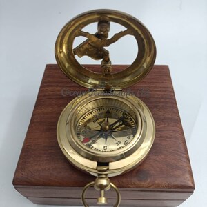 May include: A brass compass with a wooden box. The compass has a red heart on the face and a sun dial on the top.