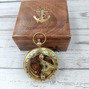 Peut inclure: Une boussole en laiton avec une boîte en bois. La boussole a un cadran solaire et une aiguille de boussole. La boîte a une ancre gravée sur le dessus et les mots "Oceanhandicraftsart".