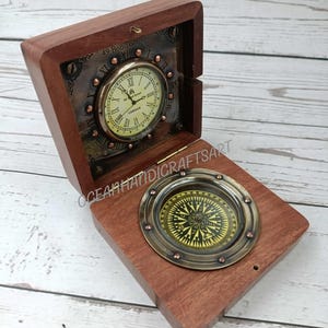 May include: A wooden box with a brass compass and a clock inside. The clock face has Roman numerals and the words "49 Bond Street London" on it. The compass has a black and gold face with a compass rose and cardinal directions.