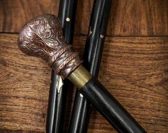 Könnte beinhalten: Nahaufnahme von drei schwarzen Spazierstöcken mit dekorativen Metallakzenten. Der Griff ist mit einer kupferfarbenen Oberfläche verziert. Der Text "Ocean Handicrafts Art" befindet sich am unteren Bildrand.
