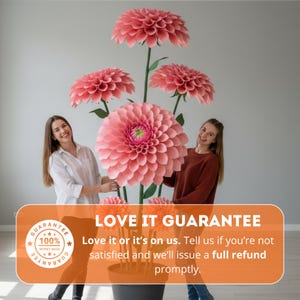 Pode incluir: Uma exibi&ccedil;&atilde;o de grandes d&aacute;lias de papel em tons variados de rosa, com caules e folhas verdes. As flores est&atilde;o dispostas num vaso, com o texto "LOVE IT GUARANTEE" e um distintivo de garantia vis&iacute;vel.