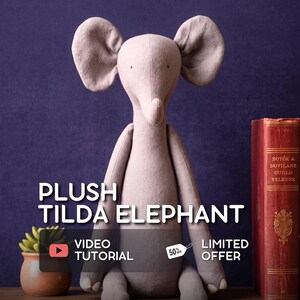 May include: A plush Tilda elephant in a soft gray color, with large ears and a long trunk. The image includes text that reads "PLUSH TILDA ELEPHANT", "VIDEO TUTORIAL", and "LIMITED OFFER". A small potted plant and a red book are also visible.