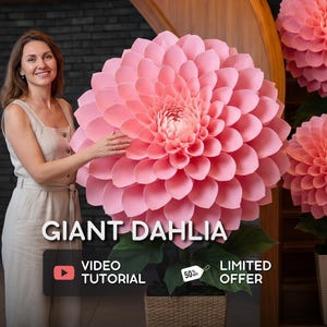 Pode incluir: Uma mulher posa ao lado de uma grande dália rosa de papel. A flor tem muitas camadas de pétalas e folhas verdes. O texto "GIANT DAHLIA" é exibido, juntamente com "VIDEO TUTORIAL" e "LIMITED OFFER". A flor está em uma cesta de vime.