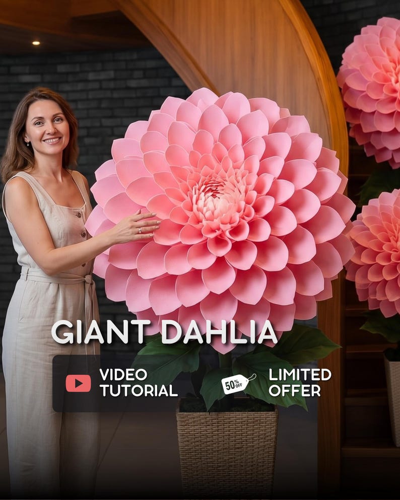 Pode incluir: Uma mulher posa ao lado de uma grande d&aacute;lia rosa de papel. A flor tem muitas camadas de p&eacute;talas e folhas verdes. O texto "GIANT DAHLIA" &eacute; exibido, juntamente com "VIDEO TUTORIAL" e "LIMITED OFFER". A flor est&aacute; em uma cesta de vime.