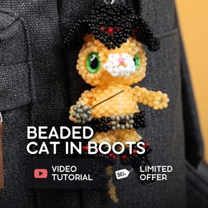 May include: A beaded cat charm wearing a black hat and boots, with green eyes and a white muzzle. The charm is attached to a silver keychain. The image includes the text "Beaded Cat in Boots" and "Video Tutorial".