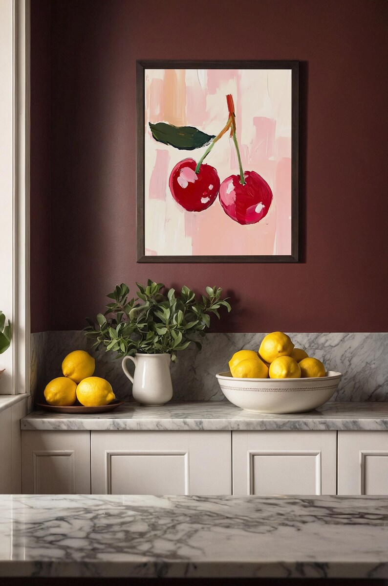 May include: A framed painting of two red cherries on a pink background with white brushstrokes. The painting is hanging on a maroon wall above a white countertop with a white pitcher and a bowl of lemons.