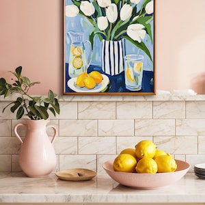 Puede incluir: Una pintura enmarcada representa tulipanes blancos en un jarr&oacute;n a rayas, con limones y limonada. Una jarra rosa y un cuenco de limones est&aacute;n sobre una encimera. La escena evoca un ambiente fresco y veraniego.