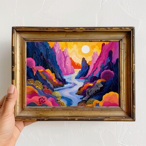 May include: A framed painting of a colorful landscape with a river winding through a canyon. The canyon walls are a mix of pink, purple, and blue, and the river is a vibrant blue. The sky is a bright yellow with a white sun.