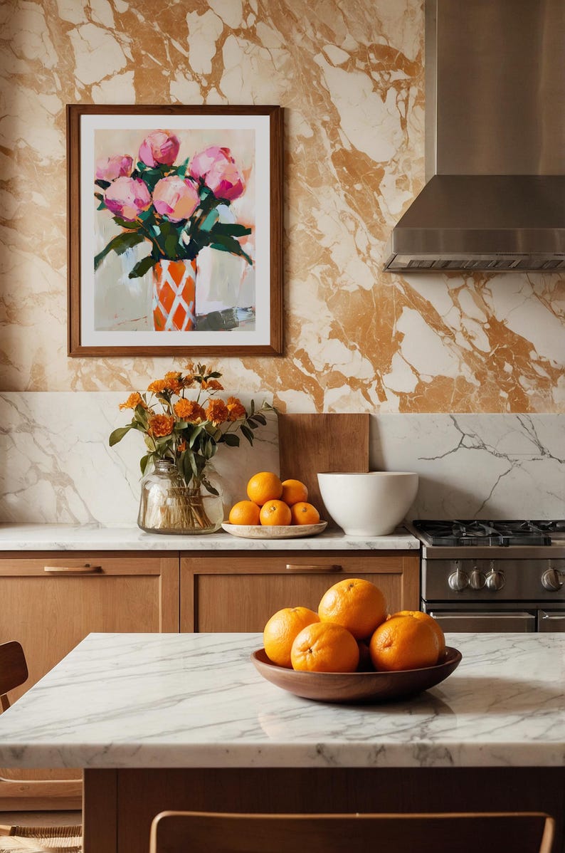 May include: A kitchen scene with a marble countertop and wooden cabinets. A framed painting of pink flowers in a vase hangs on the wall. Oranges are in a wooden bowl and on a plate.