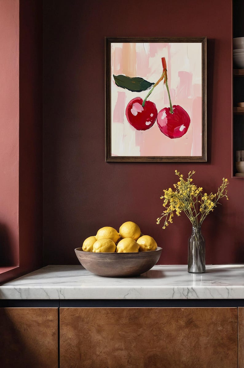 May include: A framed painting of two red cherries with green leaves on a pink and white background. The painting is hanging on a dark red wall above a bowl of yellow lemons.