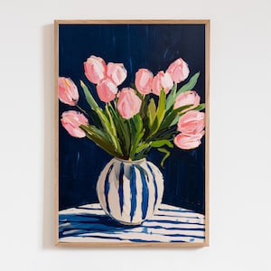 Puede incluir: Pintura enmarcada de tulipanes rosas en un jarrón blanco con rayas azules. El jarrón está sobre una superficie a rayas azules y blancas sobre un fondo azul oscuro. La obra de arte está en un marco de madera.