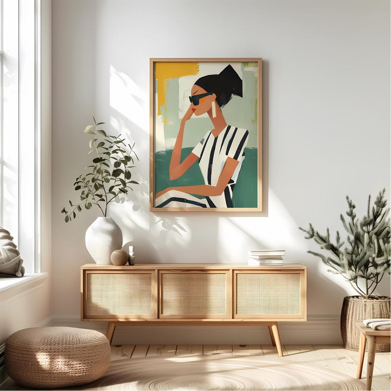 May include: A painting of a woman wearing sunglasses and a striped shirt. The woman is sitting in a chair with a green background. The painting is framed in a light wood frame.