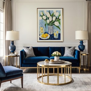 Puede incluir: Un sal&oacute;n con un sof&aacute; de terciopelo azul marino, dos l&aacute;mparas a juego y una mesa de centro con marco dorado. Una pintura de tulipanes blancos y limones cuelga sobre el sof&aacute;. La habitaci&oacute;n est&aacute; decorada con cortinas de tonos neutros y una alfombra gris.