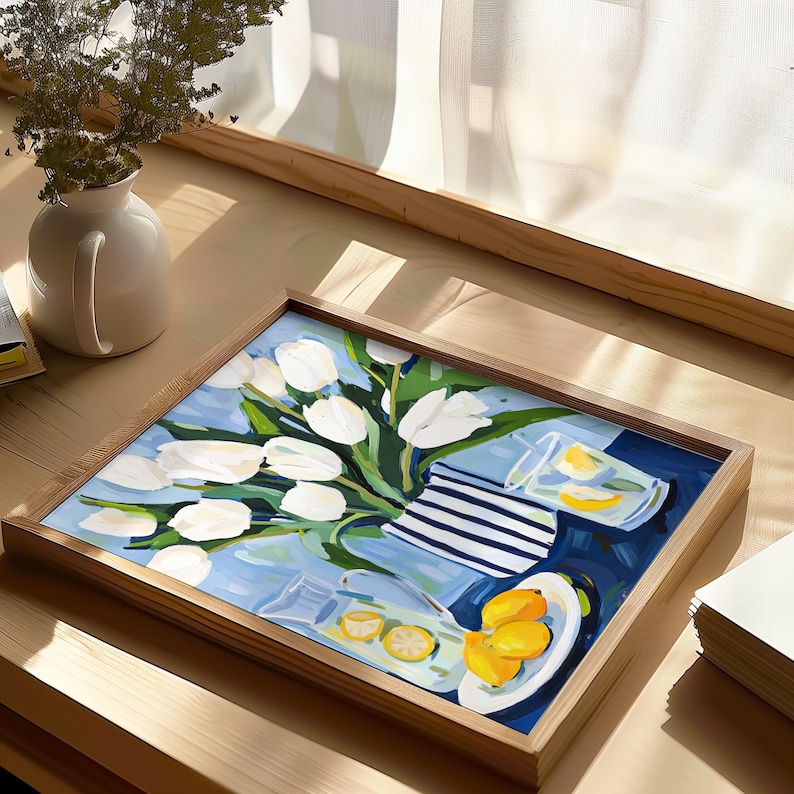Puede incluir: Una pintura enmarcada representa una naturaleza muerta con tulipanes blancos en un jarr&oacute;n, limones y vasos sobre un fondo azul. La pintura tiene un marco de madera y est&aacute; sobre una superficie de madera cerca de una ventana.