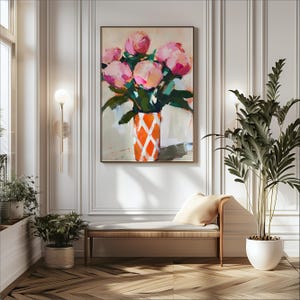 May include: An abstract painting of pink peonies in an orange and white patterned vase. The artwork is framed in a dark wood frame and hangs on a white wall. The painting is displayed in a well-lit room with a bench and potted plants.