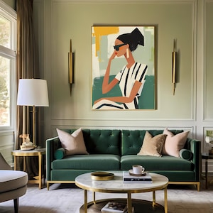 May include: A green velvet sofa with gold accents sits in a living room with a coffee table and a painting of a woman wearing sunglasses and a striped shirt. The painting is framed in gold and has a green background.