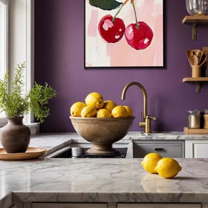 May include: A kitchen countertop with a white marble surface, a wooden bowl filled with lemons, and a gold faucet. A painting of two red cherries on a pink background hangs on the wall behind the bowl.