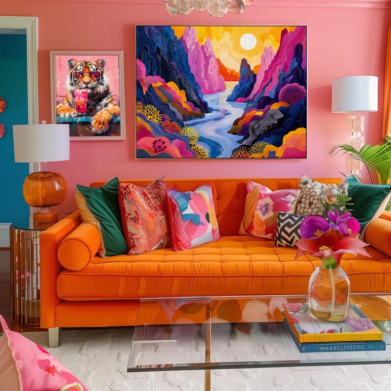 May include: A bright orange sofa with a variety of colorful throw pillows, including floral patterns and geometric designs. The sofa is in front of a pink wall with two framed pictures, one of a tiger and the other of a colorful landscape. A glass coffee table with a book on top sits in front of the sofa.