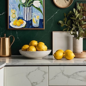 Puede incluir: Naturaleza muerta con una pintura de tulipanes blancos, limones y limonada. Un cuenco de limones sobre una encimera de m&aacute;rmol, con una jarra dorada y un reloj de madera al fondo. La escena evoca una est&eacute;tica fresca y luminosa.