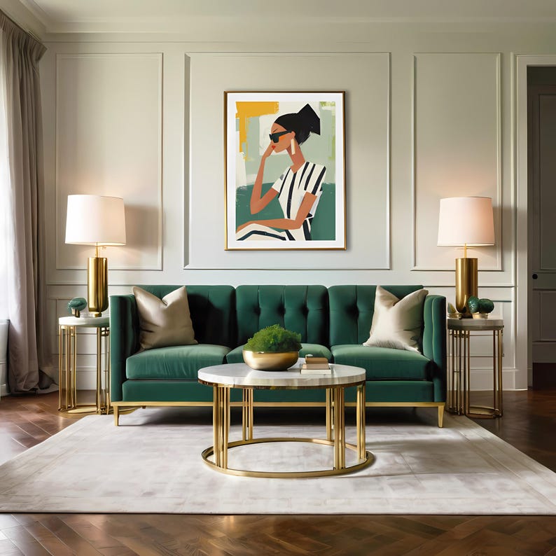 May include: A green velvet sofa with gold legs and two throw pillows sits in a living room with a gold coffee table and two gold side tables with lamps. A framed print of a woman wearing sunglasses and a striped shirt hangs on the wall.