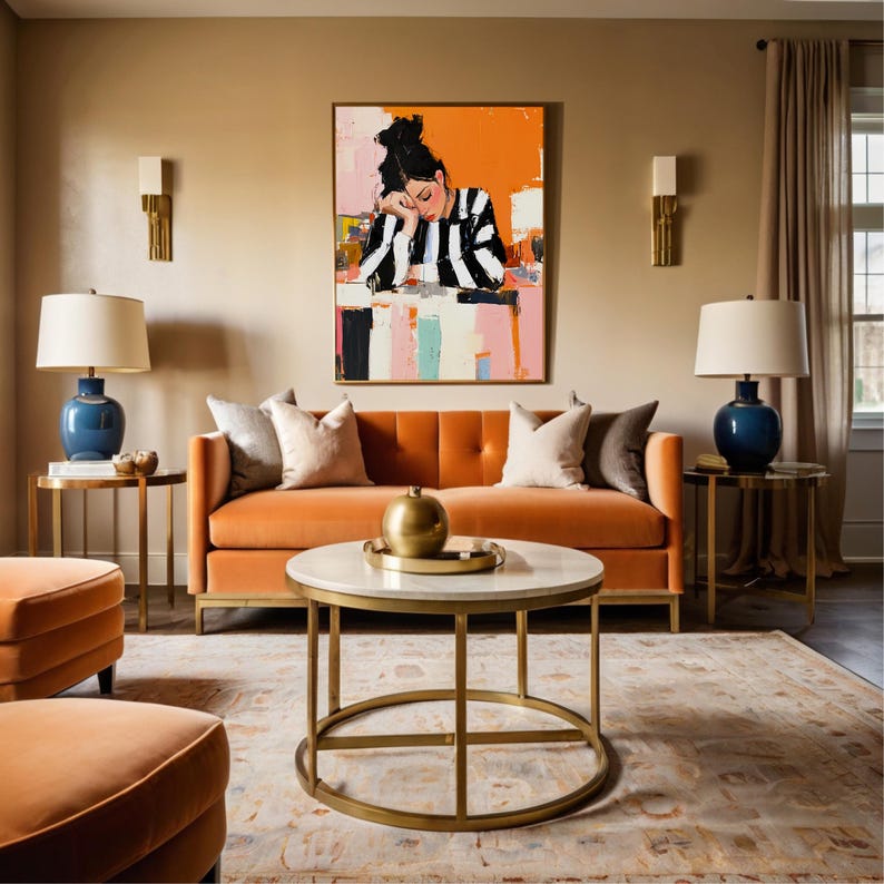 May include: A living room interior with a burnt orange velvet sofa, two end tables with gold metal frames and blue ceramic lamps, a gold metal framed coffee table with a white marble top, and a large abstract painting of a woman in a striped shirt on the wall.
