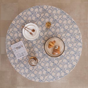 Pu&ograve; includere: Vista dall'alto di un tavolo rotondo apparecchiato per un pasto. Il tavolo &egrave; coperto da una tovaglia floreale blu e bianca. Sono visibili piatti bianchi, posate, un bicchiere di vino, un bicchiere d'acqua e un piatto con cupola di vetro con croissant.