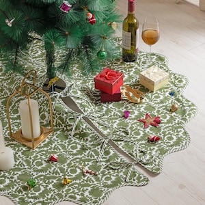 Pode incluir: Uma saia de árvore de Natal com um padrão floral verde e branco, em torno de uma árvore de Natal decorada. Uma garrafa de vinho, um copo de vinho e presentes embrulhados estão na saia. Um castiçal dourado e velas também estão presentes.